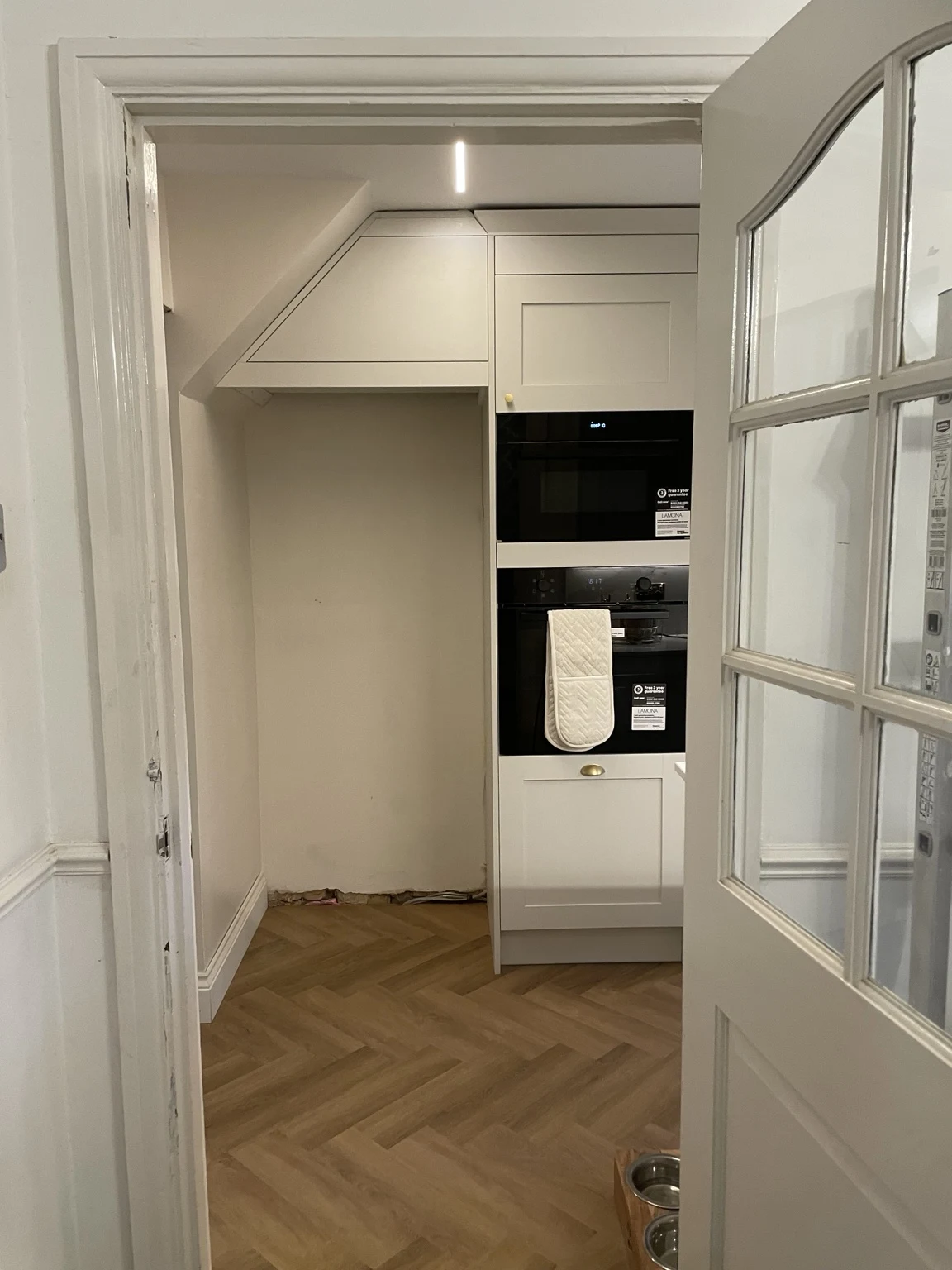 Kitchen cabinetry and built-in ovens with herringbone flooring